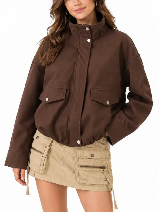 Woman wearing a brown oversized utility jacket with stand collar and snap flap pockets, styled with a beige cargo mini skirt