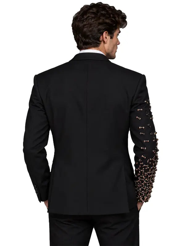 Full-length back view of men's black tailored suit featuring a clean structured jacket and embellished sleeve detail against a neutral gray studio background.