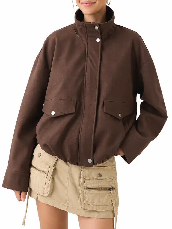Woman wearing a brown oversized utility jacket with stand collar and snap flap pockets, styled with a beige cargo mini skirt