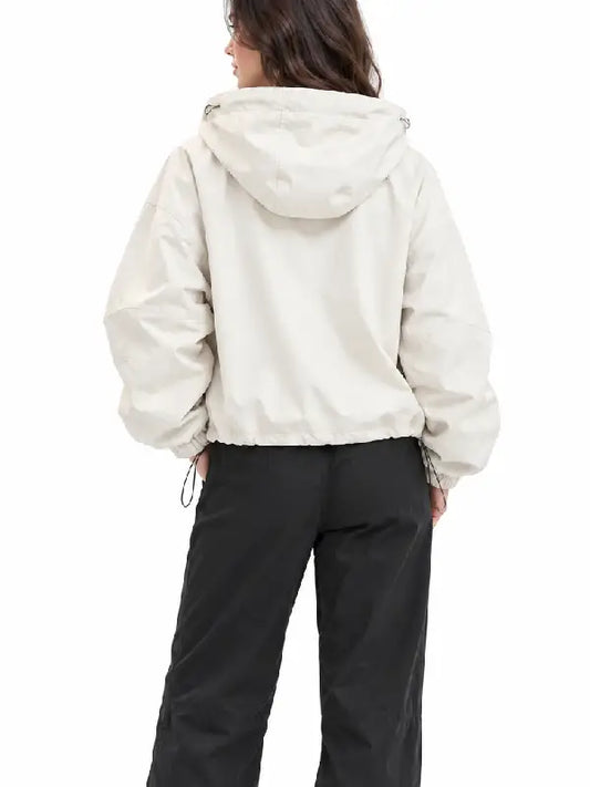Back view of a woman wearing a cream oversized hooded jacket with a drawstring hem, styled with black cargo pants