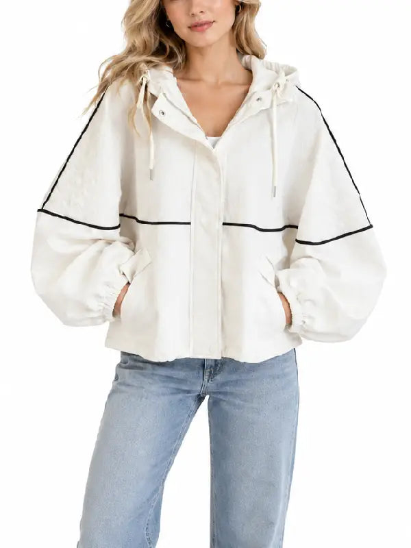 Woman wearing a cream oversized hooded jacket with black piping, front view with zipper closure and drawstring hood