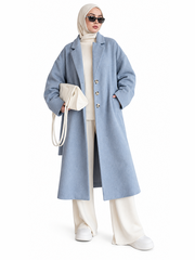 Front view of woman wearing long light blue wool coat with notch lapel and three-button front over cream knit outfit