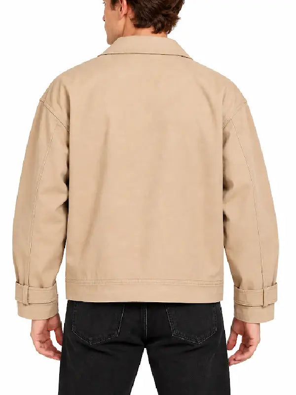 Back view of man wearing a beige chore jacket with shirt collar, button tab cuffs and black jeans