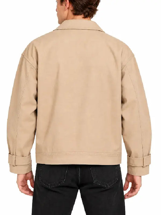 Back view of man wearing a beige chore jacket with shirt collar, button tab cuffs and black jeans