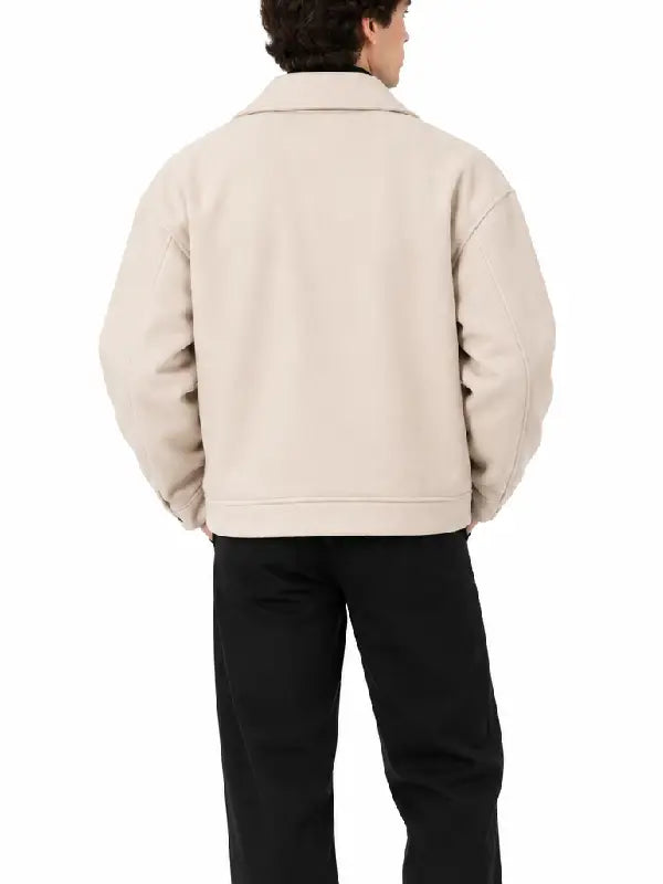 Back view of men's beige oversized biker jacket with snap button cuff tabs, worn with black trousers