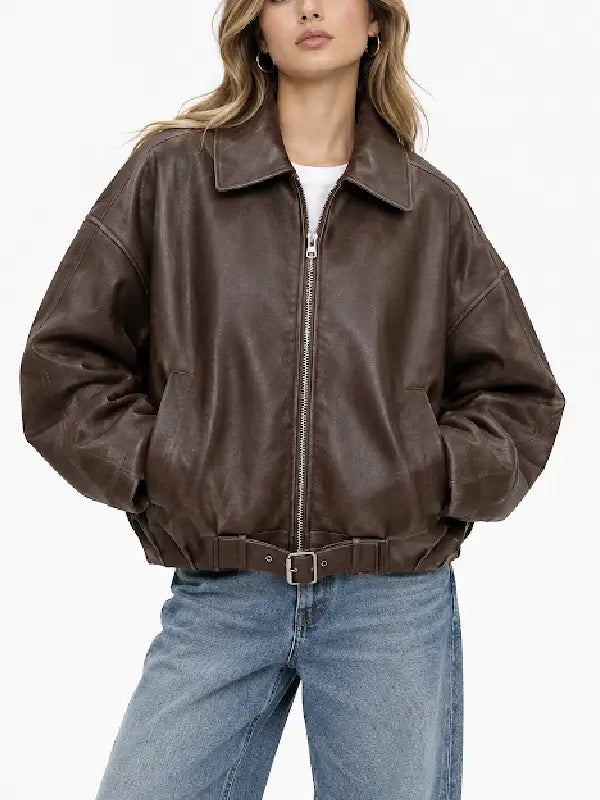 Woman wearing an oversized brown sheepskin leather bomber jacket with zip front and belted hem over a white tee and wide-leg jeans