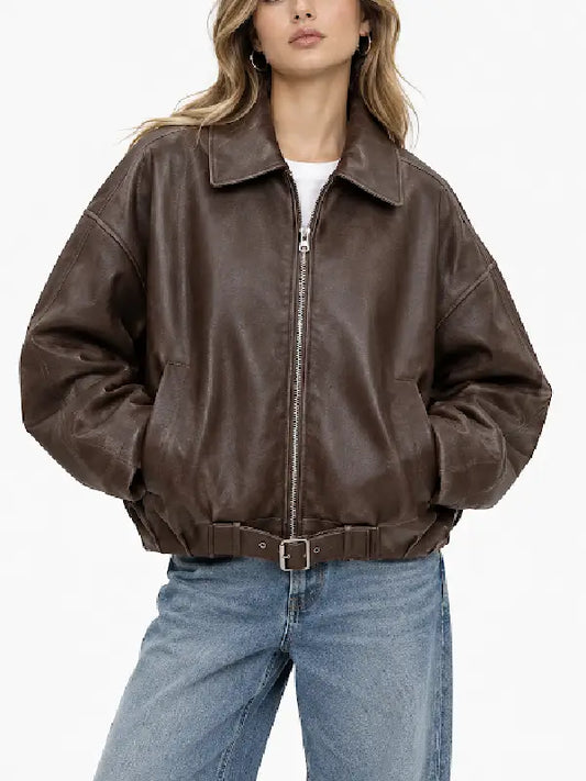 Woman wearing an oversized brown sheepskin leather bomber jacket with zip front and belted hem over a white tee and wide-leg jeans