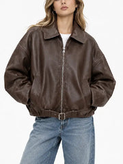 Woman wearing an oversized brown sheepskin leather bomber jacket with zip front and belted hem over a white tee and wide-leg jeans