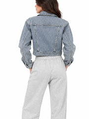 Back view of women's blue cropped denim jacket with seam detailing, worn with gray sweatpants